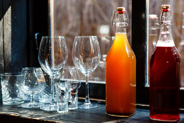 Restaurant, cafe or bar counter. Wine glasses, shot glasses, glasses for juice and water. Two bottles with non alcoholic party drinks. Beverages made of orange and red berries