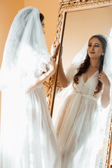 Beautiful happy bride in robe in her bedroom in a morning. The bride looks in the mirror. Beautiful...