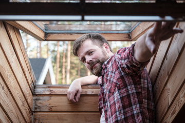Handsome bearded man stands near an open skylight in the attic.