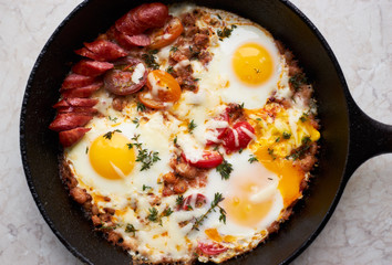 Homemade fried eggs with sausage, cheese, spices and vegetables in a pan