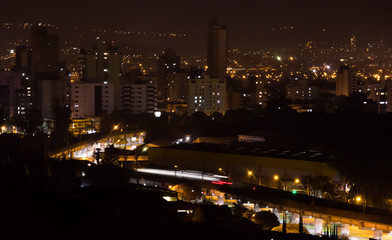Fototapeta na wymiar Night view of Sao Leopoldo City - Brasil, in the foreground the train is passing and it is possible to see only its lights due to long exposure, in the background it is the downtown