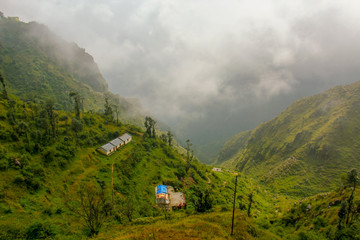 Top view of a small house/hut in the mountains. Beautiful green landscape with fog and clouds.