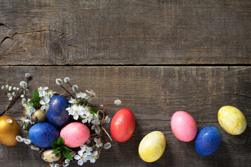 Easter eggs in a nest with willow branches and spring flowers on a gray wooden background. Top view flat lay background. Copy space.