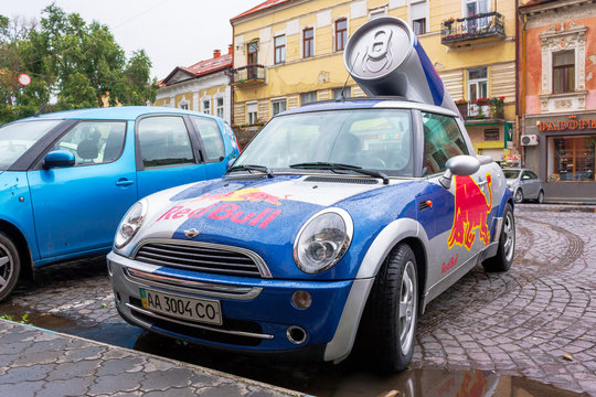 Uzhhorod, ukraine - 14 JUL, 2013: Red Bull mini cooper publicity car with a can of energy drink behind. fancy car tuning used for promotion. wet advertisement vehicle after the rain