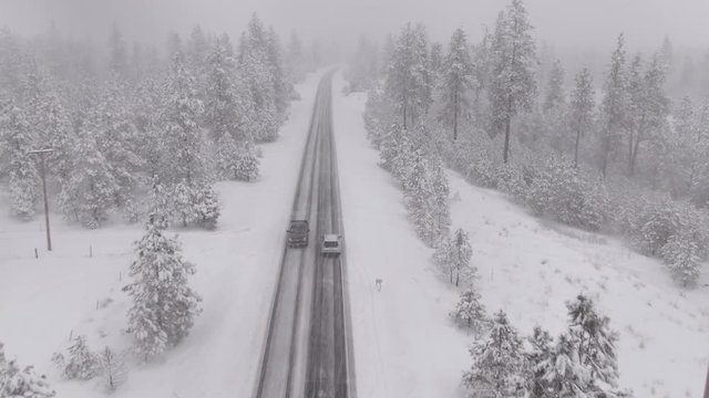 AERIAL: Commuters in cars drive through a blizzard engulfing the rugged American countryside. Flying above a slippery asphalt road as cars drive through an intense snowstorm. Bad driving conditions