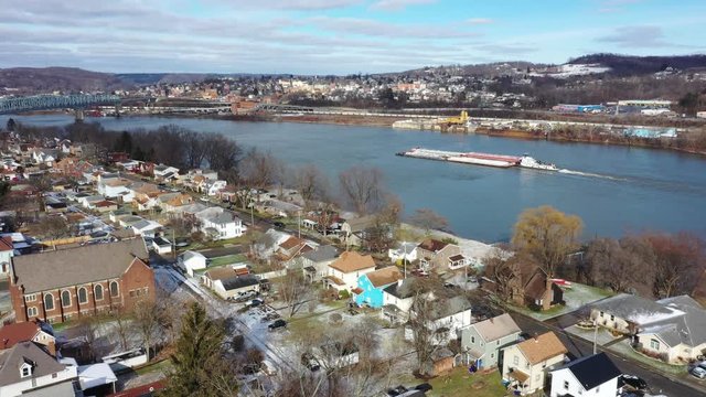 A slowly moving forward winter aerial establishing shot of the shoreline of Monaca, Pennsylvania with a coal barge on the Ohio River in the distance. Pittsburgh suburbs.  	