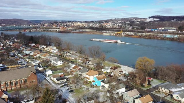 A slowly rising reverse winter aerial establishing shot of the shoreline of Monaca, Pennsylvania with a coal barge on the Ohio River in the distance. Pittsburgh suburbs.  	