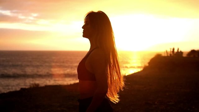 Healthy people lifestyle enjoying sunset and fitness activity alone - beautiful woman feel the sun and the ocean oxygen after workout sport session class - open arms and freedom breathe