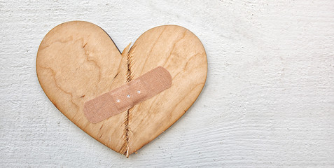 Two parts of broken wooden heart taped by a patch. Concept of the forgiveness, renewal of relations...