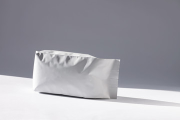Naklejka premium Blank foil food or drink bag on white background in minimal style, natural light shadow. Monochrome photo front view.Packaging valve and seal template mockup. Metallic coffee tea retail package design