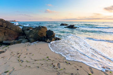 sea beach at sunrise. calm waves wash huge rocks. golden clouds on the sky. stunning marine scenery in morning light.