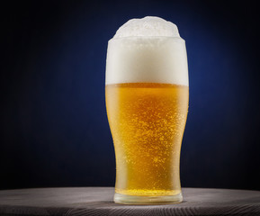A glass of cold beer with foam on a bright blue background. Space for text.