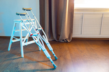 Crutches and a white stool are in the room. Crutches for hire. Rental of medical equipment. Rehabilitation of invalids. Services of a traumatologist. Treatment of leg diseases.