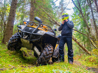 A man in a yellow helmet stands next to ATV. ATV riding in the woods. Off-road transport. The equipment of the driver of the ATV. Racing on the forest road. © Grispb