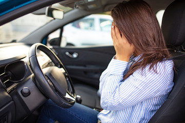 Young woman with hands on eyes sitting depressed in car. Woman driving feeling anxiety behind the wheel. Cropped shot of a young woman looking stressed-out while sitting in her car