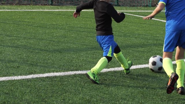 Close-up of preadolescent football player's legs skillfully dribbling soccer ball, bypassing back player and scoring goal. Active young footballer showing high skill of keeping ball during game