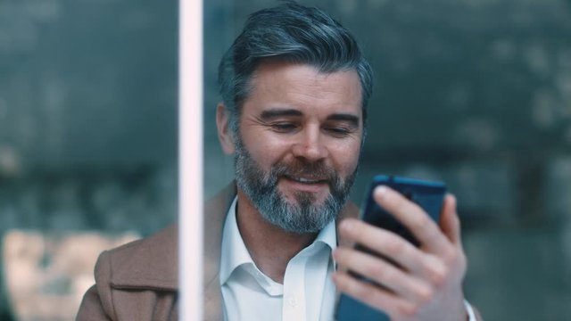 Portrait of attractive middle aged business man in the caf&eacute;, laughing at the internet memes, jokes. Modern life, being stylish. Texting to a friend. Close up view, slow motion.