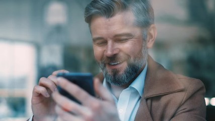 Portrait of gorgeous smiling middle aged beared business man uses phone drinks coffee at cafe texing message working successful people daily routine relaxing new technologies communicating slow motion - Powered by Adobe