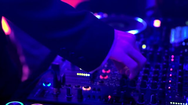 DJ hands touch buttons and sliders on sound mixing controller deck with turntables, monitors and wires, close-up. Disc jockey mix tracks, play electronic music on pro audio equipment at night club.