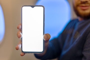 Mockup smartphone airplane. Young attractive european man holding blank screen smartphone in hands in airplane. Mock up for a game, mobile application, web site a horizontal oriental. Stock photo.