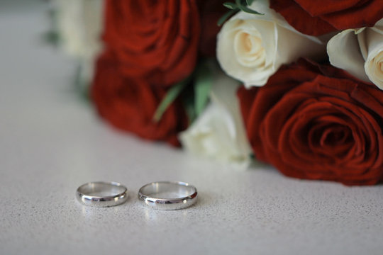 Marriage rings with bouquet of white and red roses blurred background