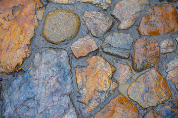 Wet stone road. Stone road texture. Cobblestone. Stones of different types. Masonry. Natural texture. Bridge. Background from the pavement. Antique road. Cobblestone bridge texture.