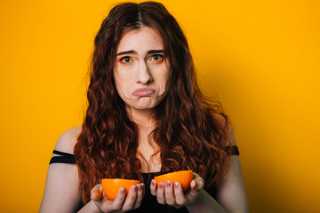 Beautiful girl on a bright yellow background. Model with fruit in hand. Two orange slices. emotion....