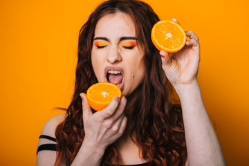 Beautiful girl on a bright yellow background. Model with fruit in hand. Two orange slices.  emotion. Crooked faces