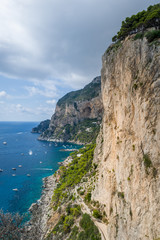 Fototapeta na wymiar Vertical photo of rocks and cliffs of Capri island. Viewpoint to the sea bay with small local's boats and perfect climbing walls. Capri, Italy.