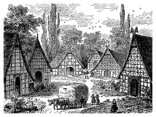 Idyllic view of North German rural village with half-timbered facades immersed in great vegetation and a cart of hay pulled by oxen