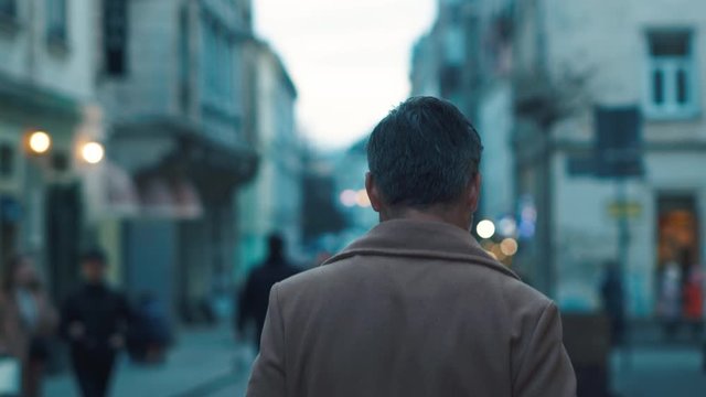 Back view of unrecognizable man walks along the city center street looks around city lights on background business downtown evening happy close up slow motion outdoor