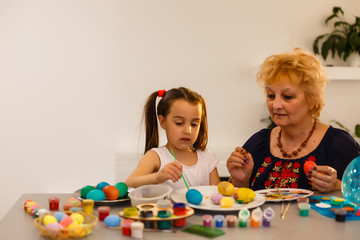 Naklejka premium Grandmother with granddaughter are coloring eggs for Easter.