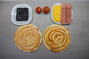 pizza preparation process top view: two round blanks of pizza dough with salami olives, cheese on...