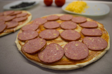 two round pizzas with salami cheese and olives tomatoes and sauce and on a gray table with texture top view