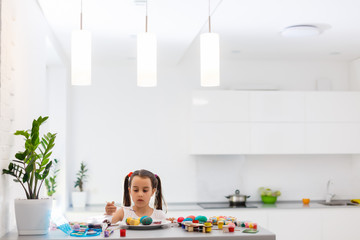 Little girl painting Easter eggs in the kitchen