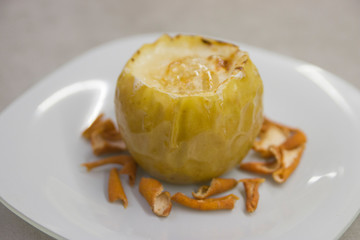 author's dish: baked apple with sugar syrup on top and grapefruit zest on the sides on a white plate on a gray kitchen table close-up