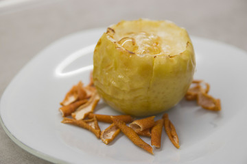 author's dish: baked apple with sugar syrup on top and grapefruit zest on the sides on a white plate on a gray kitchen table close-up