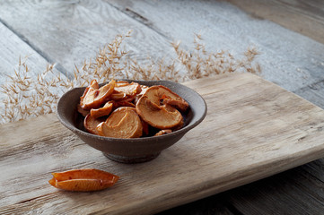 Dried Apple slices in a ceramic plate stand on a textured wooden Board, next to a dried Apple in the form of a boat.Horizontal layout, copy space. Apple chips.
