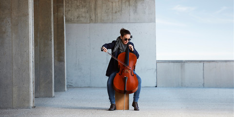 beautiful girl plays the cello with passion in a concrete environment
