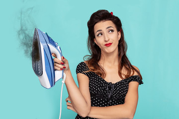 Young woman in pin-up style holding a burning iron and  looks bored