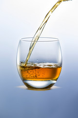 Whiskey pouring from the neck of a bottle into a glass on a wooden stand