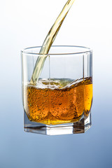 A stream of whiskey from a bottle fills a glass cup