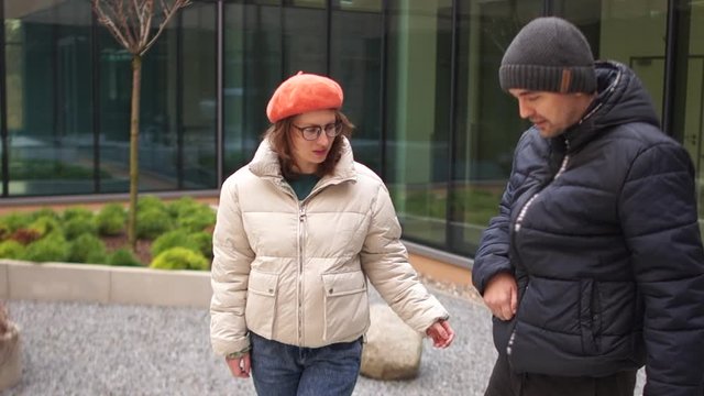 Young man in a black jacket and hat learns to walk again after a stroke or accident. Paralysis of extremities. Nearby is his girlfriend, a woman in a white jacket