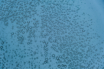 Fototapeta na wymiar Raindrops on Transparent Glass Surface on a Cold Snowy Winter Background