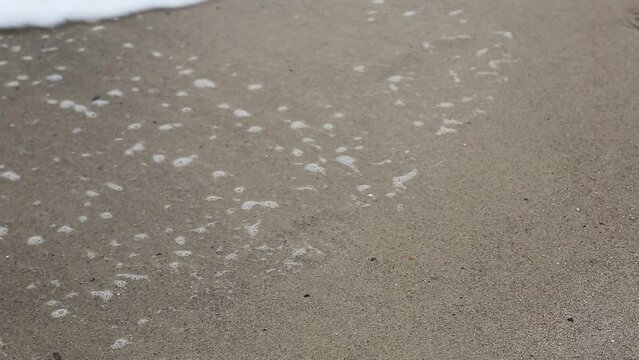 Foamy splashing sea tide waves washing over on the sea sand coast.