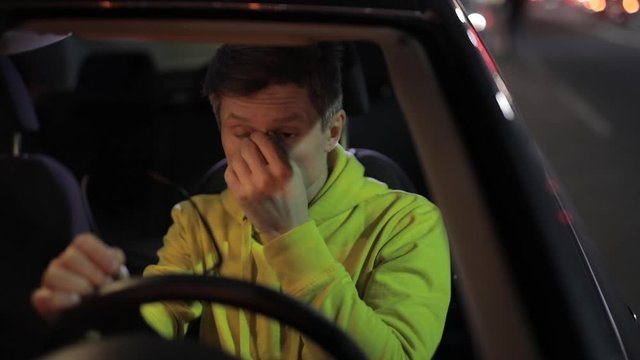 Tired man driver want to sleep but try on yellow eyeglasses in the car and ready to drive