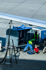 An employee of the ground service of the airport operating the tanker refills the aircraft with aviation fuel. Other workers load luggage into the plane.