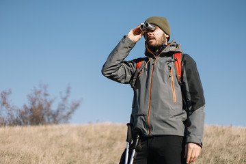 Man with hiking equipment searching direction using binocular