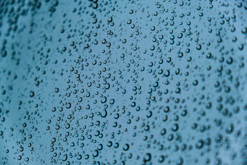 Raindrops on Transparent Glass Surface on a Cold Snowy Winter Background