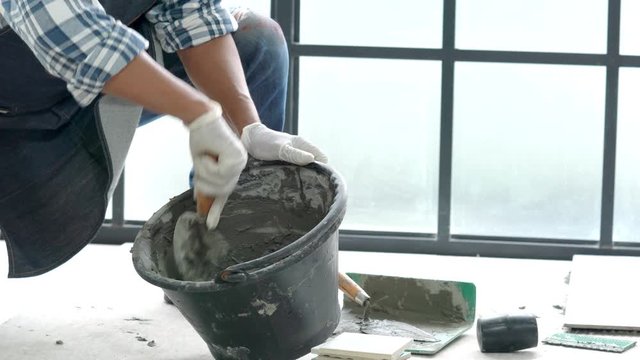 4K Senior man worker working at construction site using trowel mixing concrete cement mortar in bucket for preparing home renovation repair work or tile paving floor. Elderly man diy working concept.